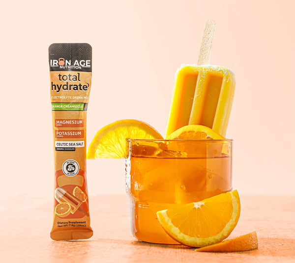 Iron Age Nutrition Total Hydrate electrolyte powder in Orange Creamsicle flavor, showing a vibrant orange drink with powder packaging.