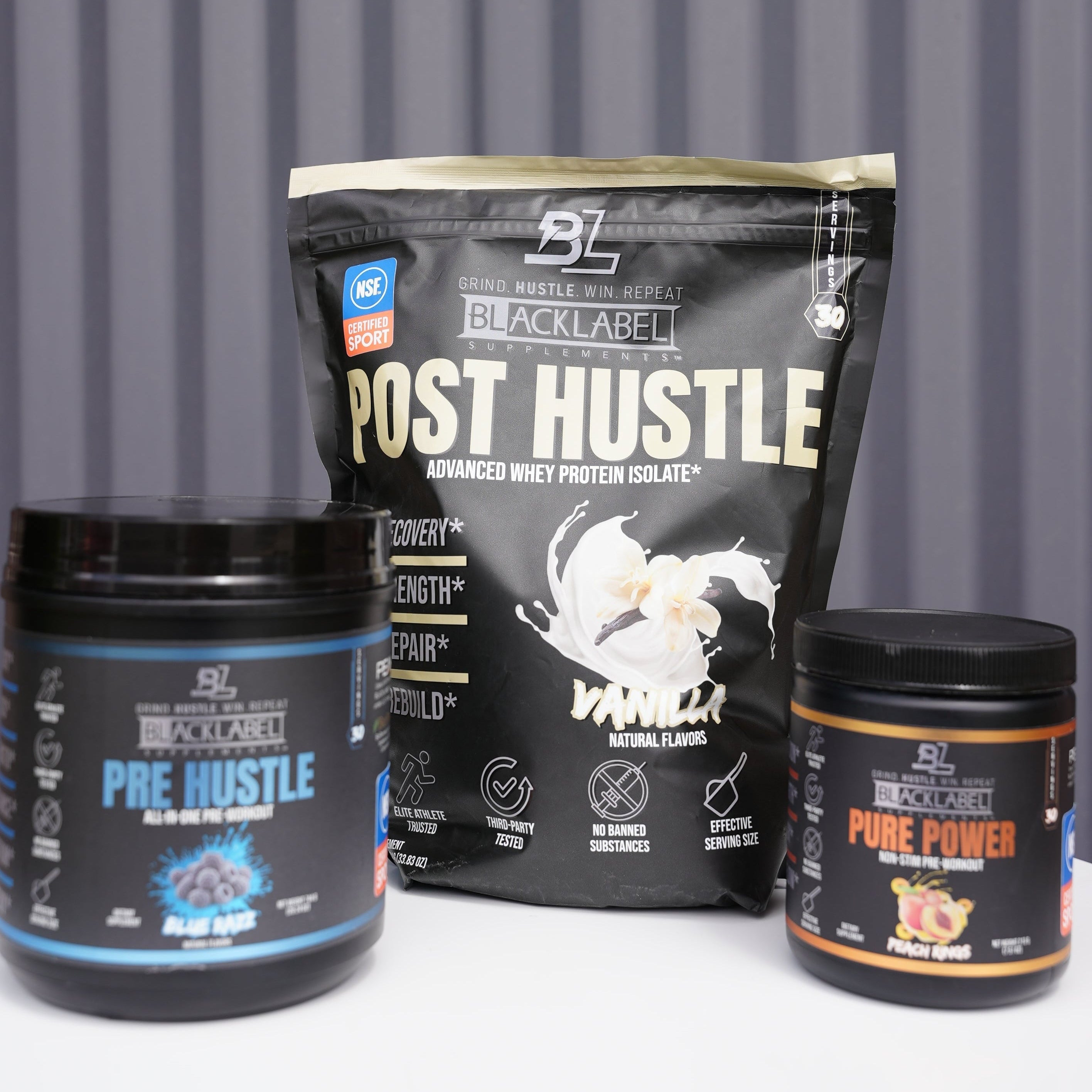 BlackLabel Supplements Post Hustle protein powder, Pre Hustle pre-workout, and Pure Power supplement bottles on a white surface.