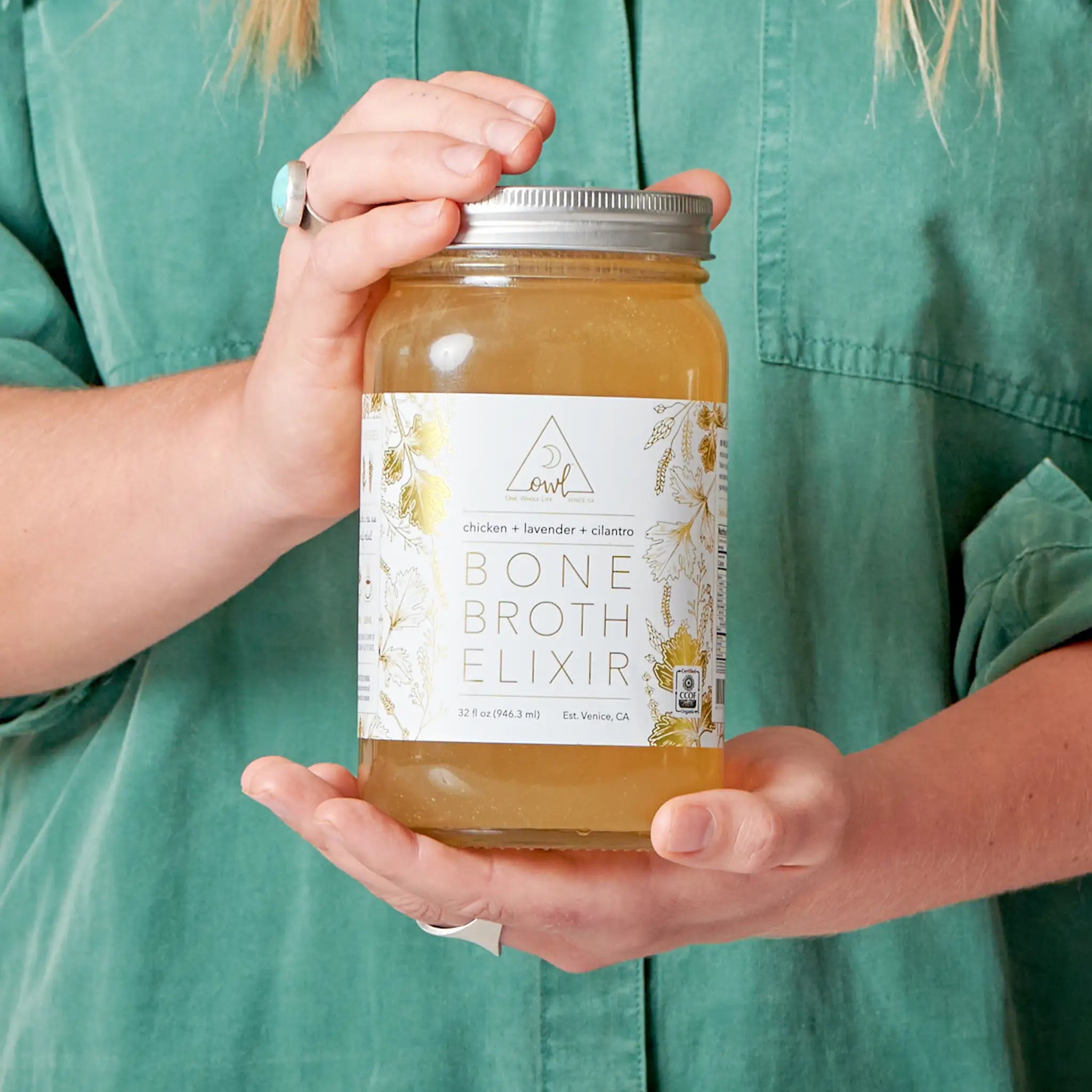 Organic chicken bone broth elixir by OWL Venice, showing a jar of nourishing, clear bone broth with fresh chicken bones and herbs.