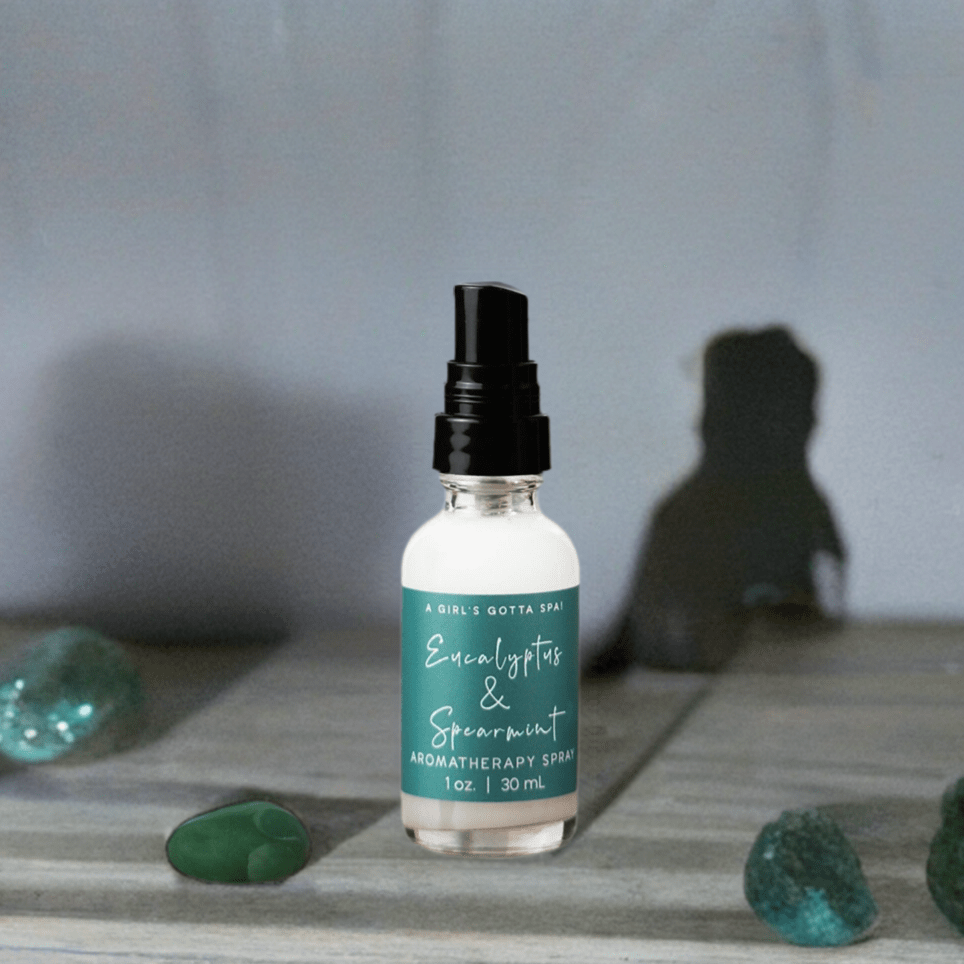 A Girl's Gotta Spa! eucalyptus and spearmint aromatherapy spray in a glass bottle with a spray nozzle, surrounded by fresh herbs.