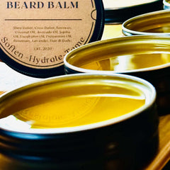 Restalgic Atelier luxury beard balm in a 2oz jar, showing a sleek black container with a gold lid and natural beard care ingredients